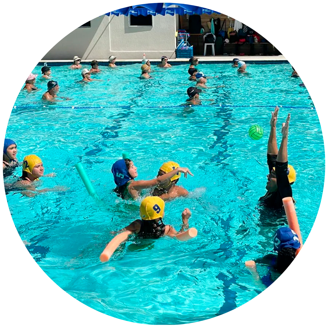 Grupo de crianças animadas a jogar polo aquático com uma bola verde durante as atividades complementares de natação infantil na piscina da academia Acqua Fitness, no Recreio dos Bandeirantes.
